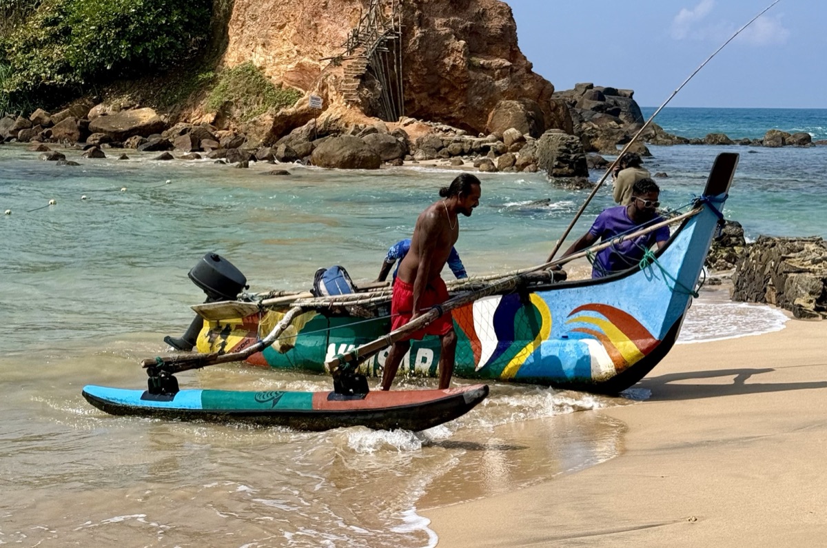 Fishermen launching a traditional outrigger fishing boat from the beach